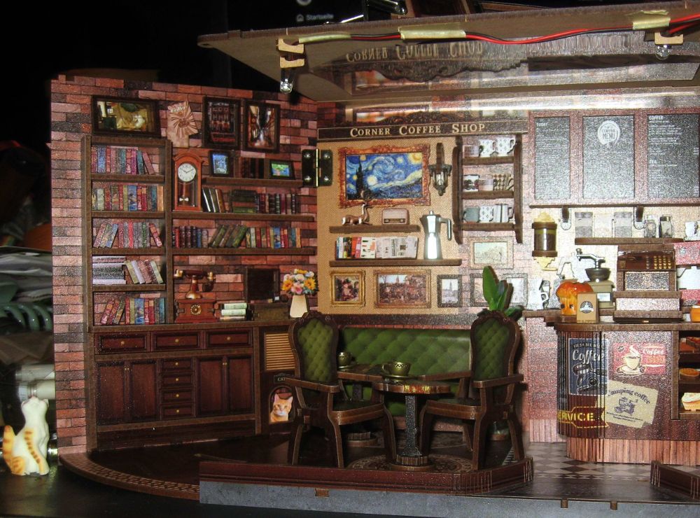 Foto zeigt ein halbfertiges BookNook, ein kleines Diorama, eines Coffee Shops. An den Wänden hängen viele, sehr kleine, Bilder.