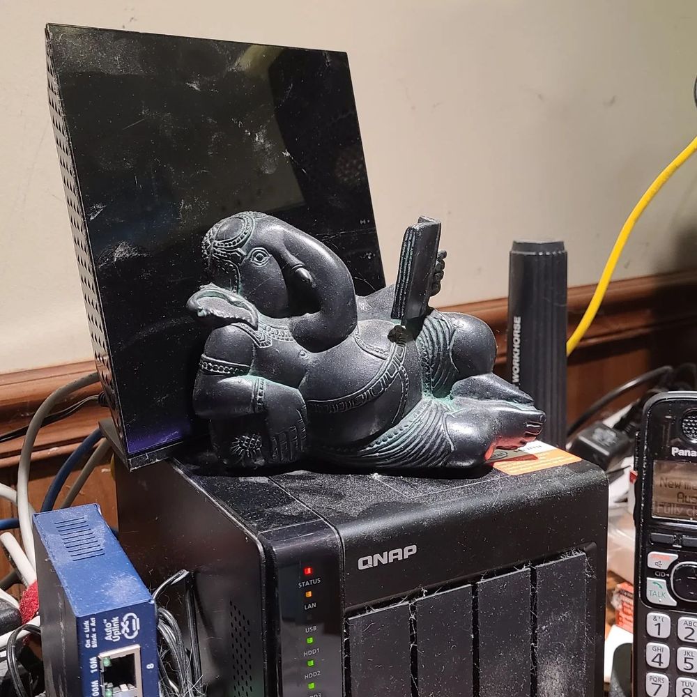 Statue of a resting Elephant headed deity - Ganesha - Remover of Obstacles - resting on a QNAP 4 slot file server and in front of a Netgear router. 