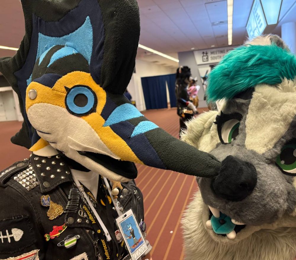 A photo of me in my marlin fursuit, with it’s long nose squeezed into the nostril of another fursuit 