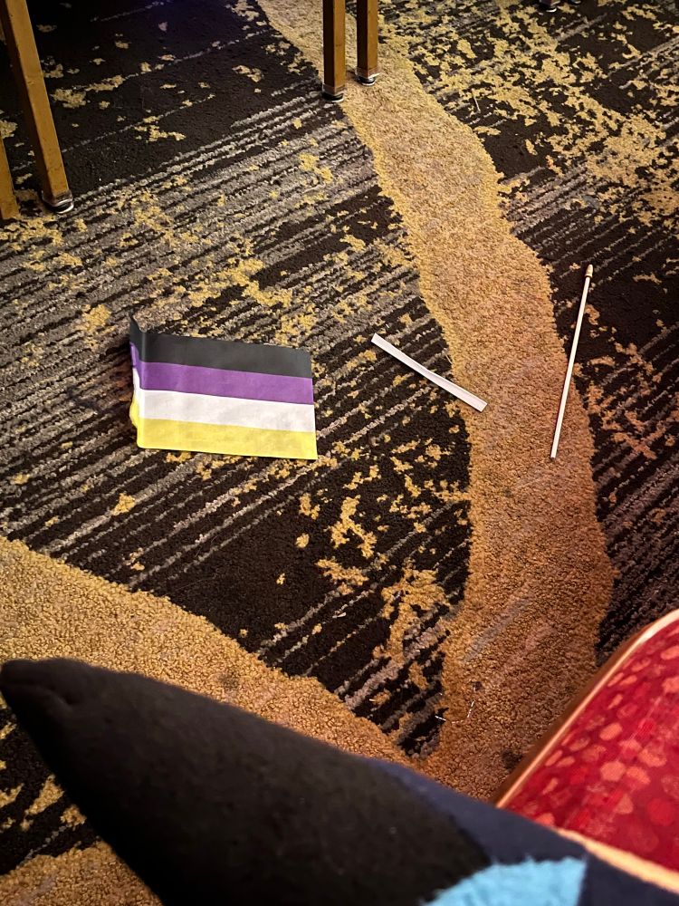 A photo of a broken nonbinary flag on the floor in a public place 