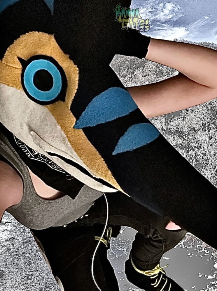 An edited photograph of me with my marlin fursuit head on looking closely at the camera. There is a heavily edited photograph of nature behind me