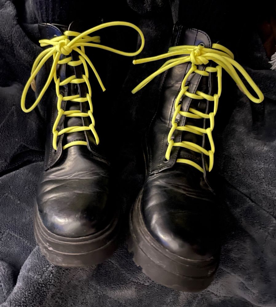 A pair of black boots, with yellow parachute chord for laces, tied ladder laced.