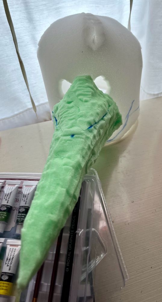 A “bucket head” type base for a first head with a long nose roughly sculpted from green foam attached to it.