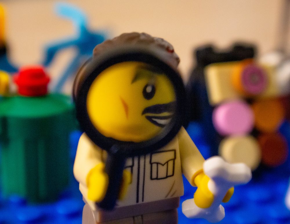 A macro photo of a Lego archaeologist holding a bone and examining something through a magnifying glass