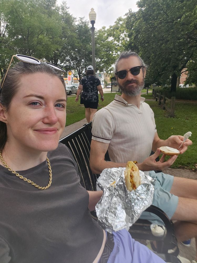 Two people eating breakfast on a park bench