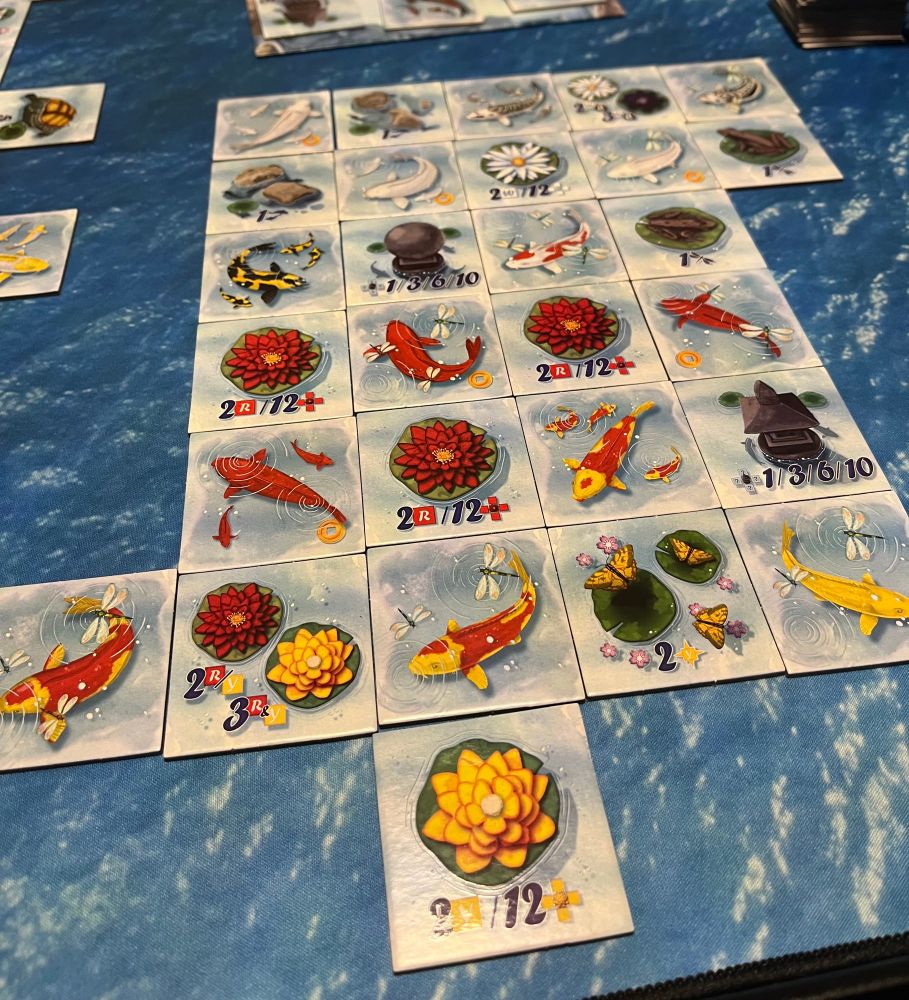 My finished tableau of tiles alternating koi fish with pond features. The koi fish are generally grouped by colors of yellow, red, white and black. Most of the feature tiles are flowers of the same colors with frogs, butterflies and statues mixed in. 