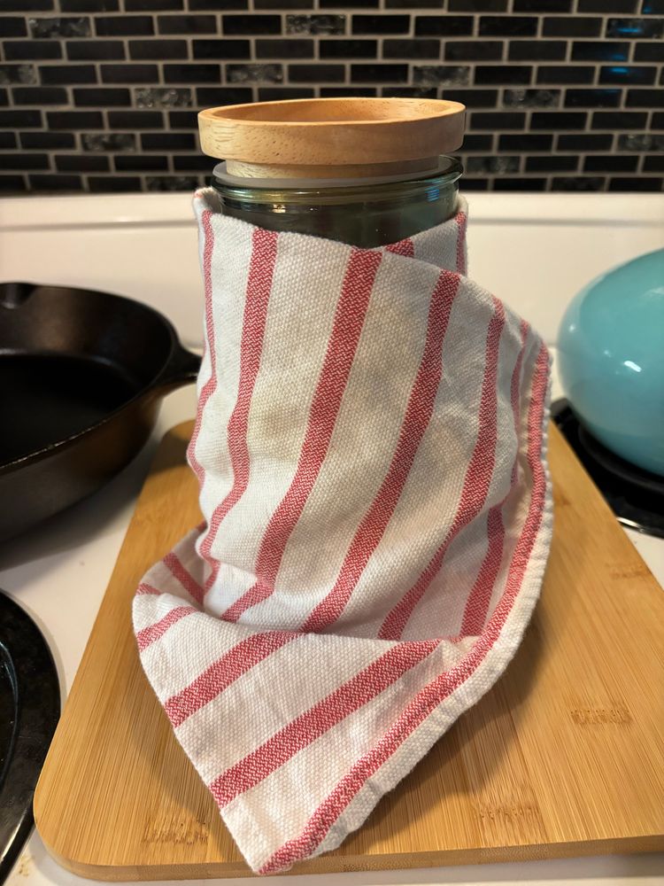 Jar of sourdough starter wrapped in a tea towel