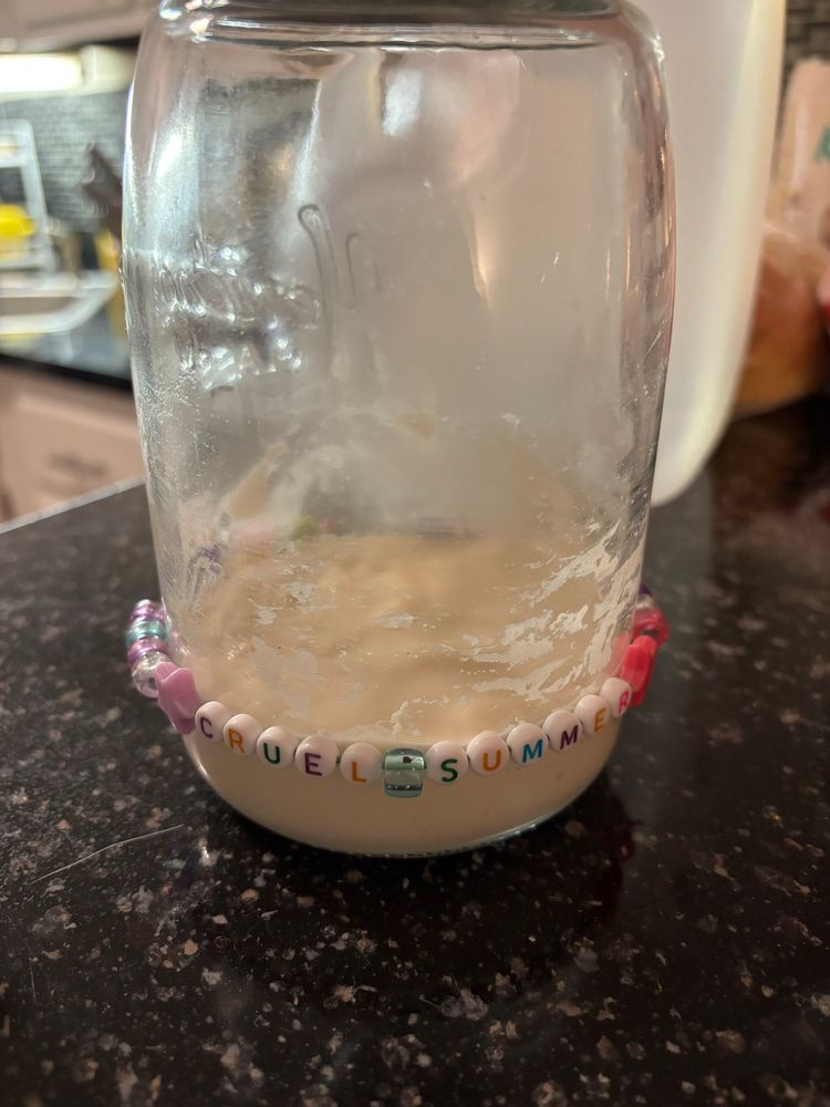 Sourdough starter in a jar with a friendship bracelet around it that says “cruel summer”
