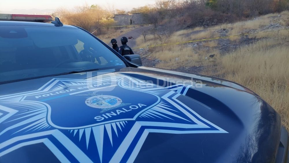 Unidad de policía en primer plano. 

En el fondo se puede ver un pequeño bulto que es el cadáver del difunto. 