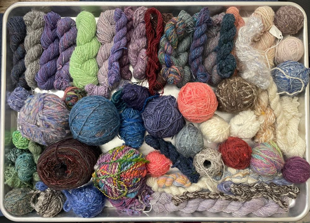 A large baking sheet fills the frame, full of small skeins and balls of yarn in a variety of colors and textures. The yarn is handspun and full of character. #handspinning #yarn 