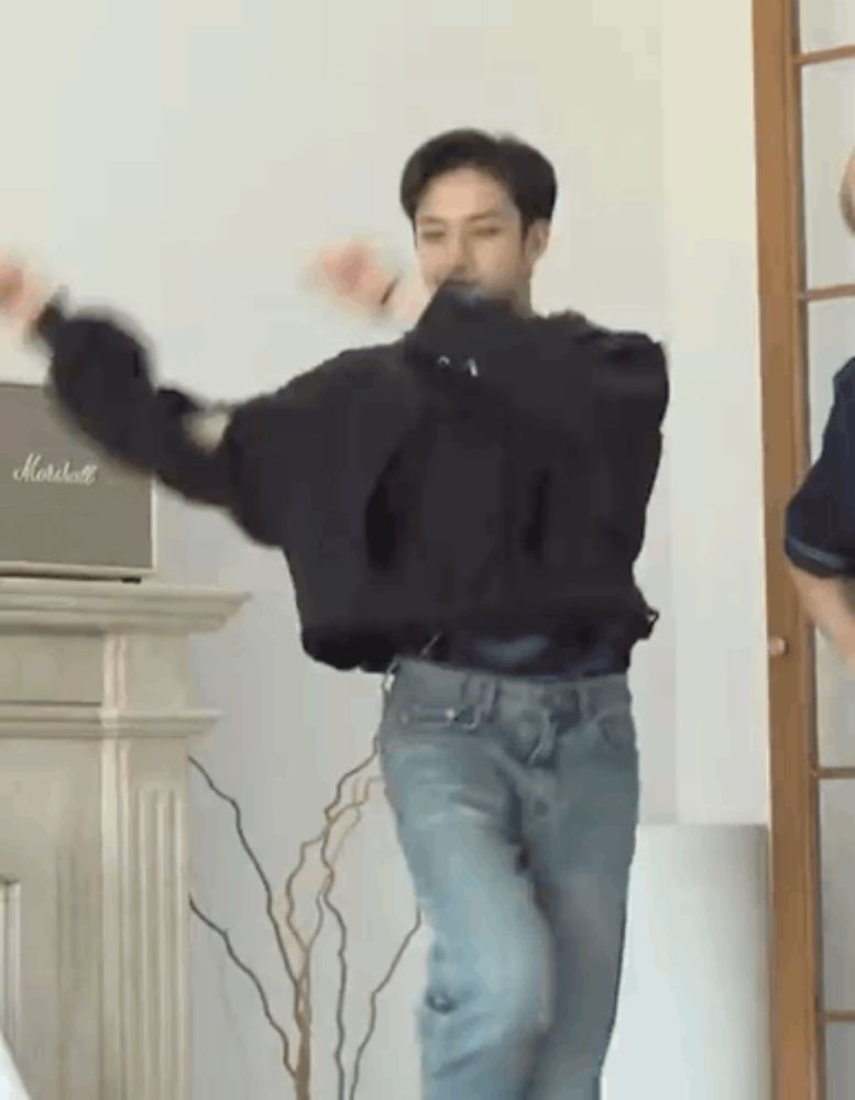 a man in a black sweater and blue jeans is dancing in a room with a marshall speaker in the background .