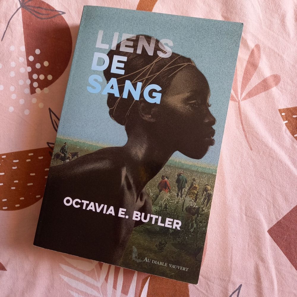 Roman "Liens de sang" d'Octavia Butler, édité au Diable Vauvert. La couverture montre une femme noire, le haut du corps nu et les cheveux dissimulés sous un fichu, devant un champ de coton dans lequel travaillent des esclaves noirs sur la supervision d'un homme blanc à cheval
