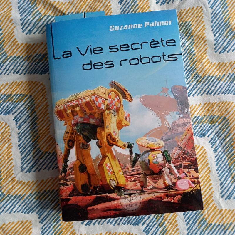 La vie secrète des robots de Suzanne Palmer, un roman paru aux éditions du Bélial'. La couverture montre deux robots se tenant par la main, un grand et un petit, au milieu de débris, avec deux grandes paraboles en fond. Le petit robot tient un doudou rose dans une de ses mains.