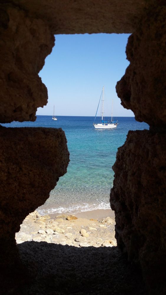 Blick durch eine Maueröffnung auf das Meer, zwei Segelboote.