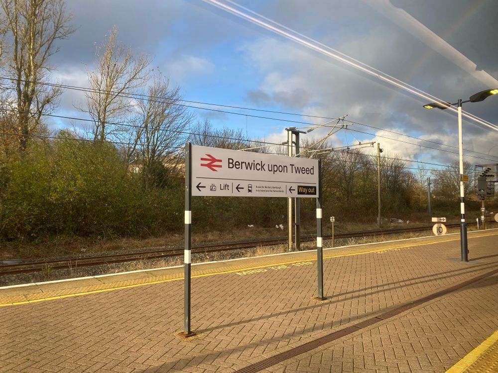Railway sign reading Berwick upon Tweed. Sky is six eighths occluded. 