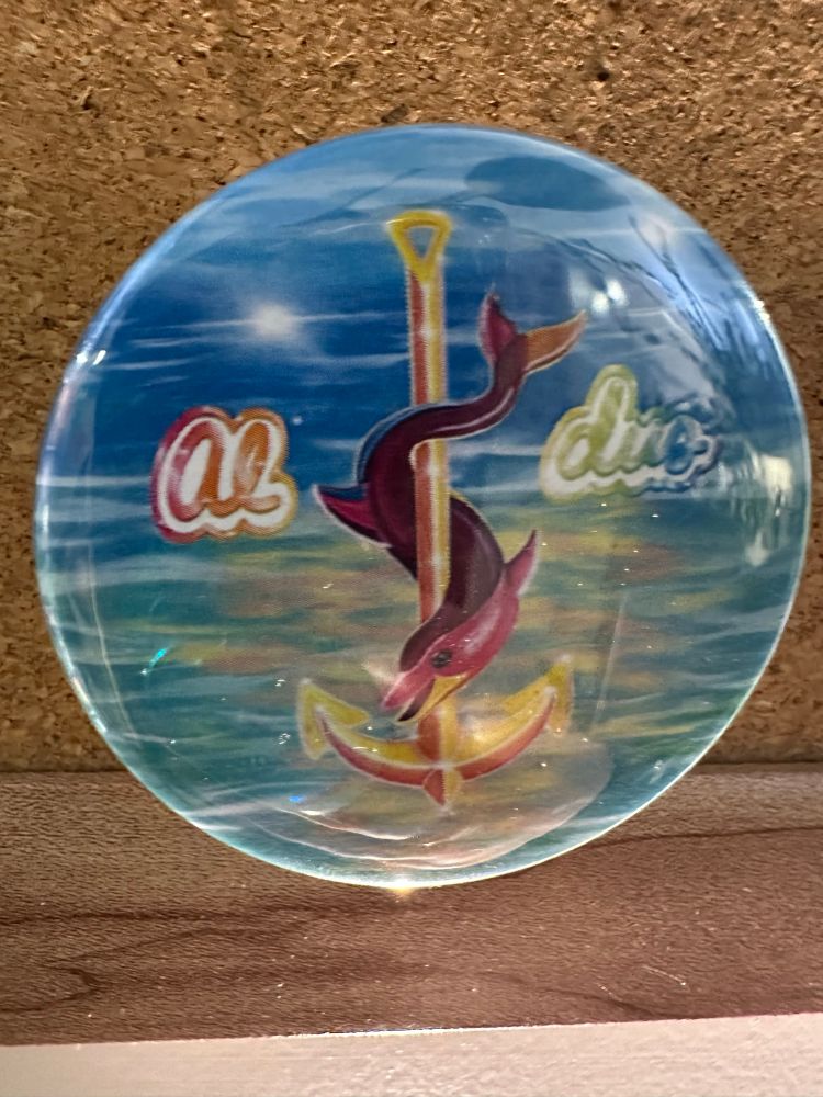 Picture of a button with a brightly colored dolphin wrapped around an anchor and the word “Aldus” all in a Lisa Frank style 