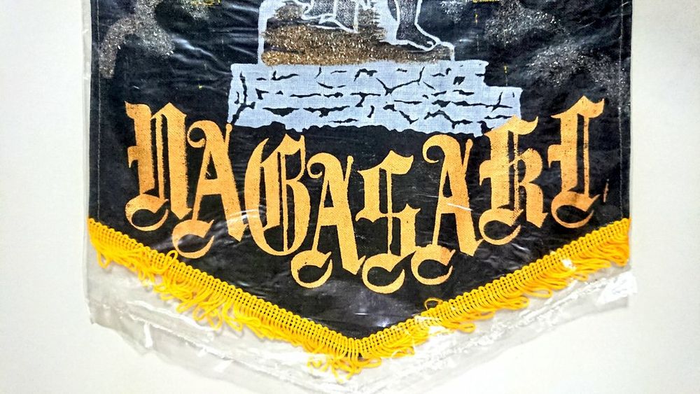 4, バナー下部。平和祈念像は台座の部分から比較的にリアルに描かれている。タイトルはローマ字。クラシックな装飾体で "NAGASAKI" （金色）。