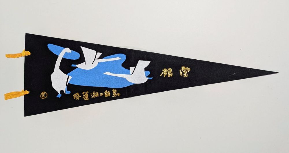 1. Nemuro, Lake Furen pennant. It features an illustration printed on black fabric, with two orange ribbons attached to the left side of the flag.