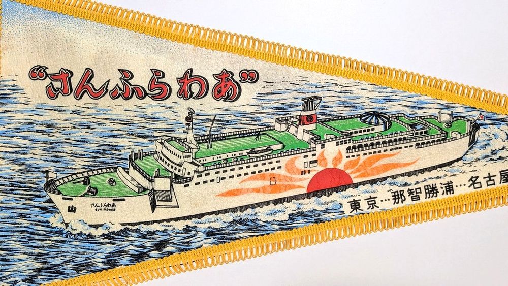 3, イラストの拡大。海をゆく”さんふらわあ’の側面全体、斜め上からの様子。船体に描かれた大きな太陽のマークや船首横のランプなど、船体の特徴がよく分かる。イラストのモデルは”さんふらわあ”, ”さんふらわあ2” か。