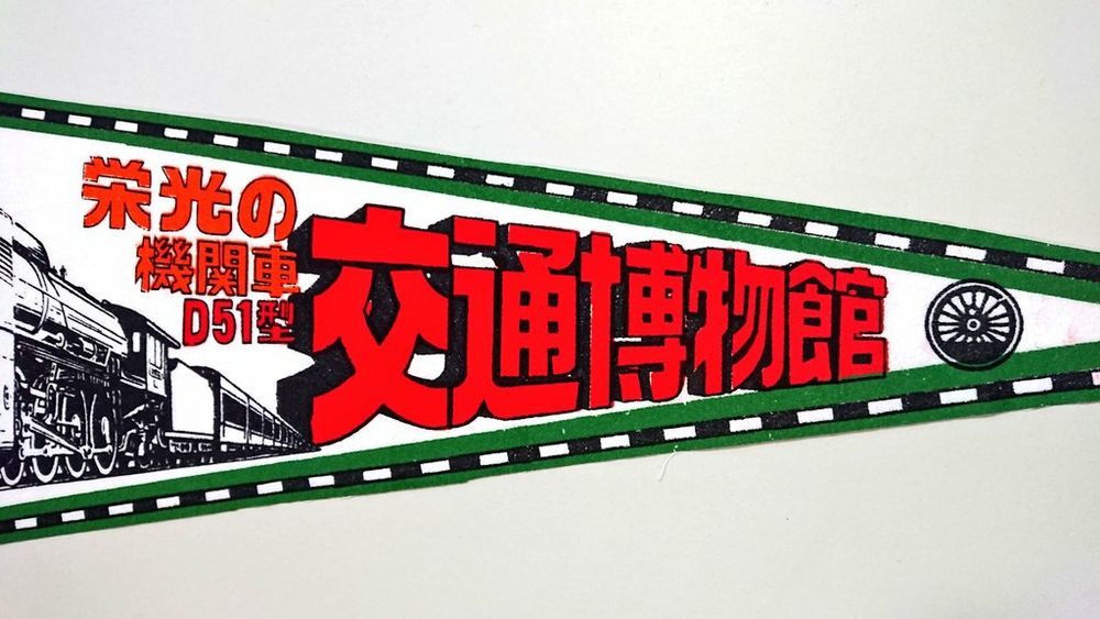 4, タイトルは和文。アレンジされた漢字で "交通博物館" （赤）。キャプションは "栄光の機関車 D51型" （橙, 赤）。ペナントの右端に蒸気機関車の動輪のイラスト （黒） が加えられている。これは"国鉄の動輪マーク"として親しまれている意匠である。