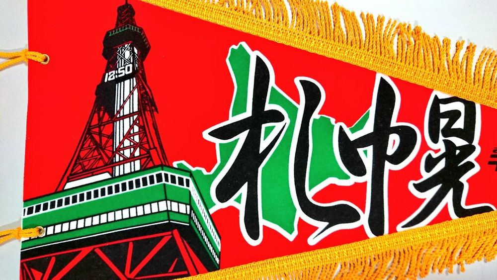 3, イラストの拡大。内藤多仲の設計によるテレビ塔、塔の足元から仰観する構図。赤い塔体と緑の展望台が鮮やか。背景に北海道の輪郭 （緑）。