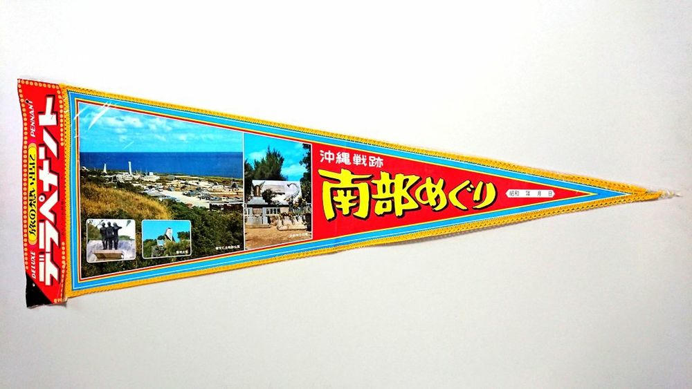 1, 沖縄戦跡、南部めぐりのペナント。紙に写真をプリント。黄色いモール装飾付き。旗はオリジナルの透明ビニル袋入り、紙のタグ付き。タグのタイトルは和文、"旅の想い出に デラペナント"、"DELUXE PENNANT, あなたのお部屋に コレクションに " （赤, 黄, 白）。