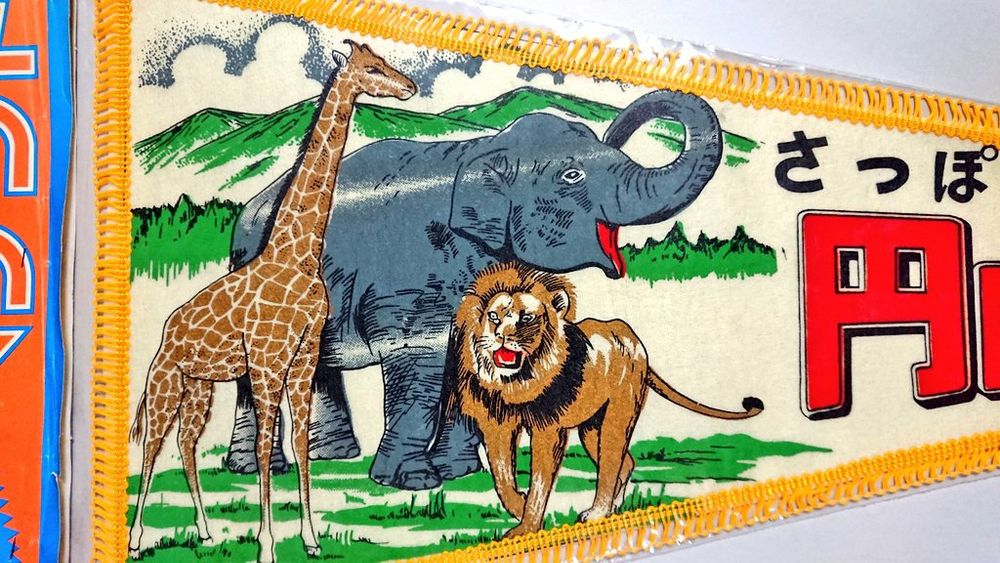 3, イラストの拡大。山々を背景にしたサバンナのように広々とした風景。動物は野生の姿らしい生き生きとした表情のキリン、ゾウ、ライオン。