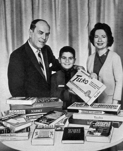 A promotional photo of John Scarne with two other people, possibly his family, featuring the games Teeko and Scarney, along with many books and other products.
