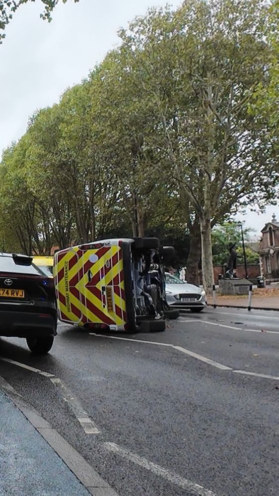Photo of a highway maintenance van in the middle of an urban road, turned on its side