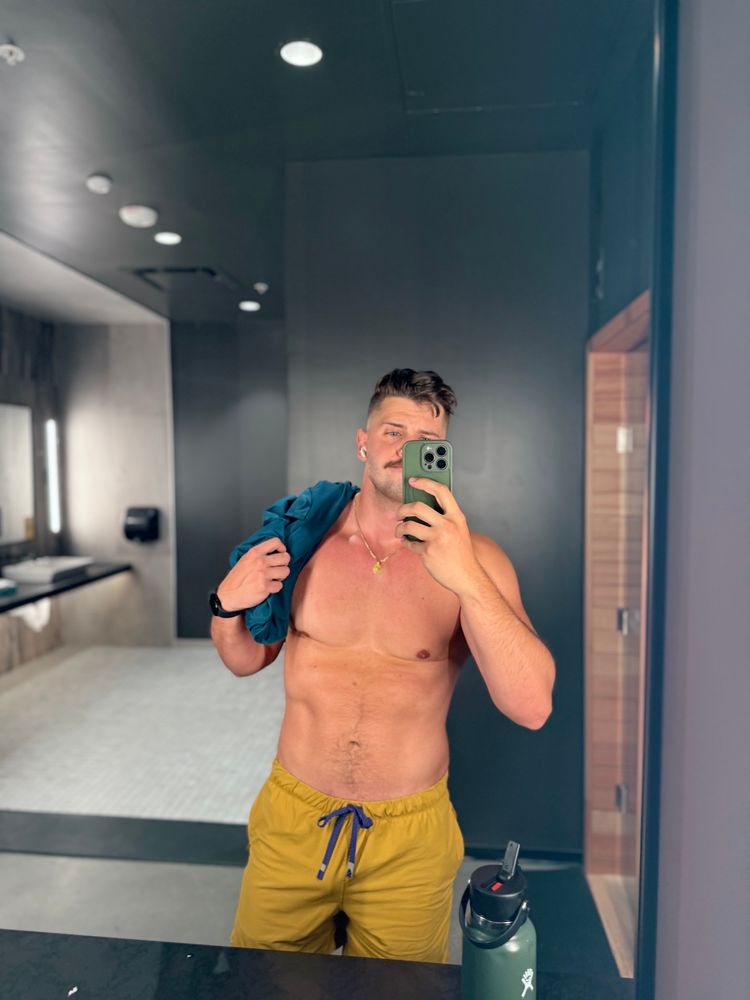 Mirror selfie of Adam (Lemonboy) after a workout. He’s in yellow shorts and his teal tank is draped over his shoulder.