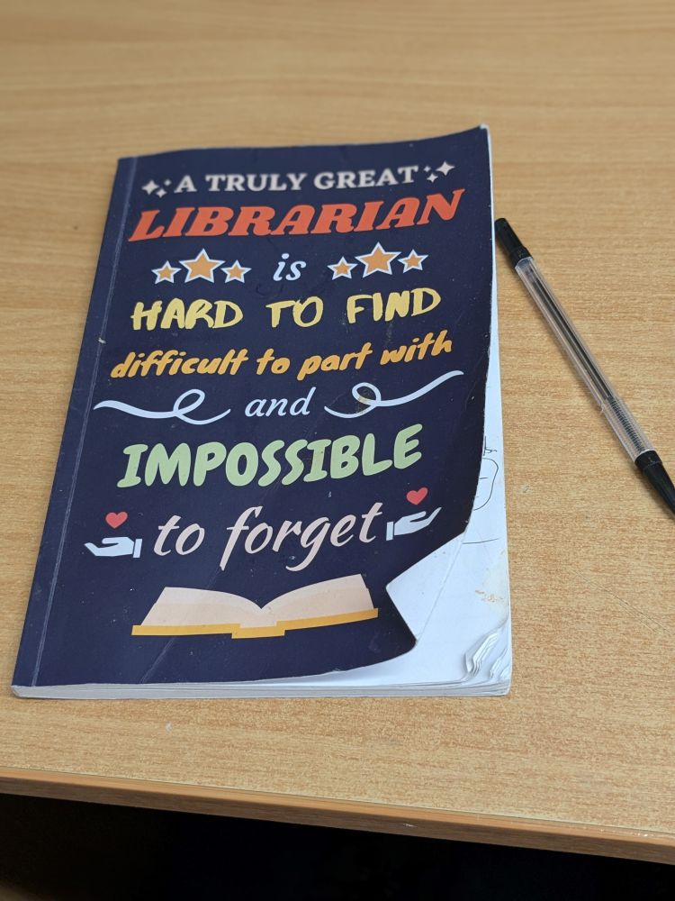 A well worn navy notebook with 'A truly great librarian is hard to find, difficult to part with and impossible to forget' written on the front.