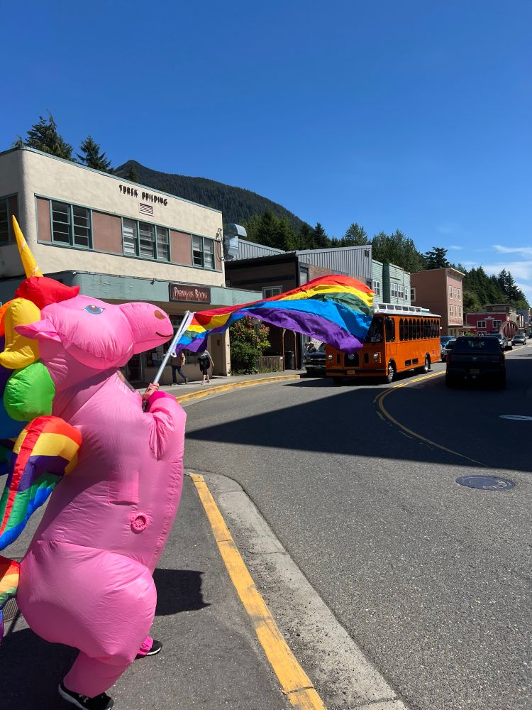 A pink unicorn waves a rainbow flag. 