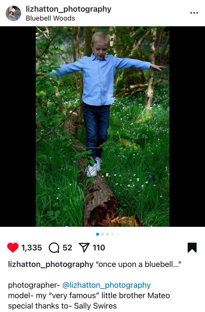 Photograph of a young boy aged 7 balancing on a fallen log in a bluebell wood. Arms outstretched to keep his balance. 