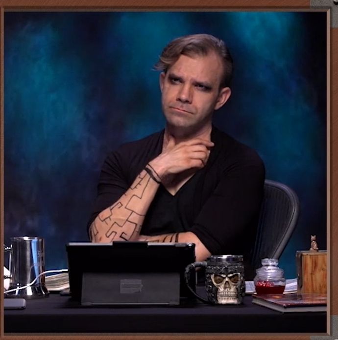 Screen shot of Liam O'Brien in costume as Astrid Becke for a Halloween episode of Critical Role. His hair is swept to the side and he is wearing dark eyeliner with a geometric pattern drawn on his arms.