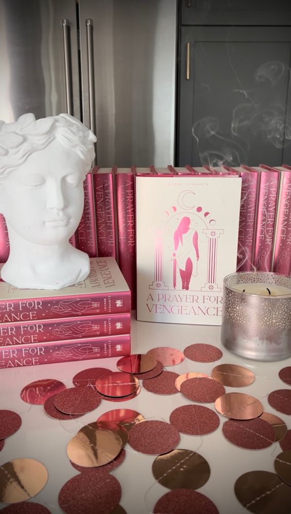 Stacks of my book with a shiny garland, candle, and plaster bust of an girl