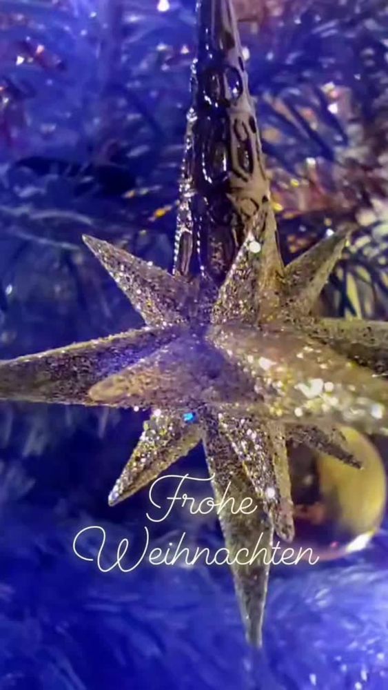 Bsumschmuck aus Glas mit Glitzeroberfläche in Form eines achtrahligen Sterne an einem Weihnachtsbaum mit Text Frohe Weihnachten
