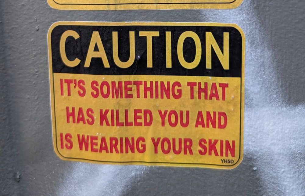 Caution sign sticker saying "Caution: It's something that has killed you and is wearing your skin"