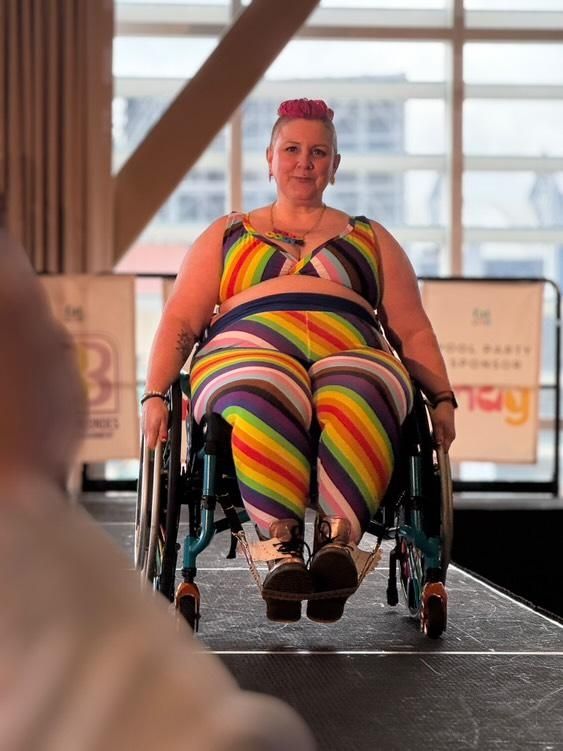 Kirsty is in a wheelchair on a Catwalk wearing Molke bra and leggings in a pride fabric design.