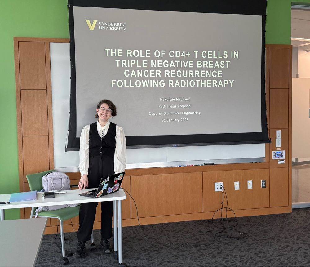 Grad student standing in front of their qualifying exam proposal title slide, smiling because they passed