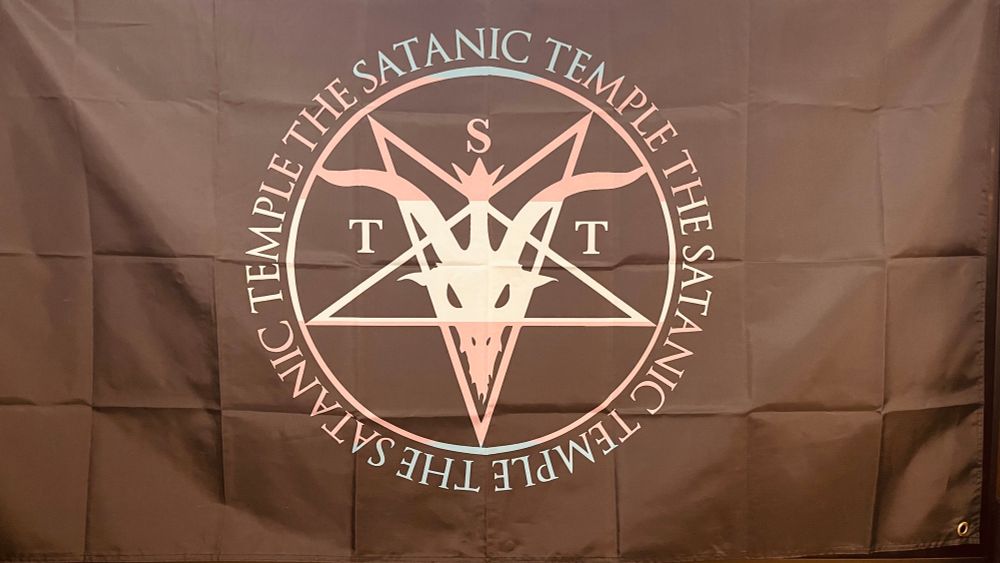 A flag from The Satanic Temple with the TST logo in the colors of the trans flag.