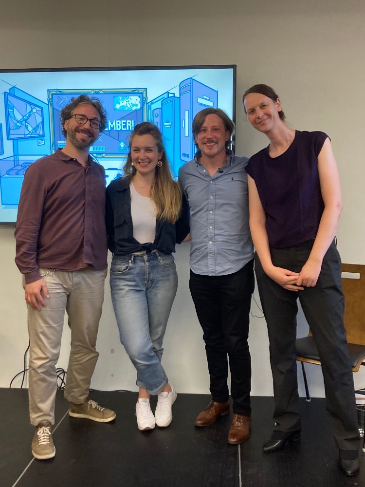 Gruppenfoto auf Bühne vor Screen mit Let's Remember Logo. Von links nach rechts: Christian Huberts (Stiftung Digitale Spielekultur, hat die Spiele gespielt), Mona Brandt (Paintbucket Games, Gesprächspartnerin, Lead Game Designerin The Darkest Files), ich, Lara Keilbart (Journalistin/Moderation). (Nicht im Bild, aber vor Ort: Tabea Widmann und Matej Samide). Danke auch an die Mitarbeitenden der Gedenkstätte Roter Ochse, Halle (Saale) für die Gastfreundschaft.