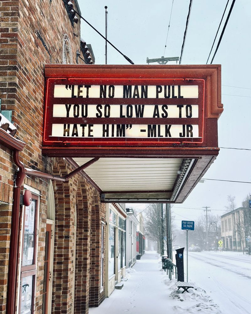 Snowy day, historic theatre red marquee on side of brick building. Letters on marquee reading: “Let no man pull you so low as to hate him - MLKJR”