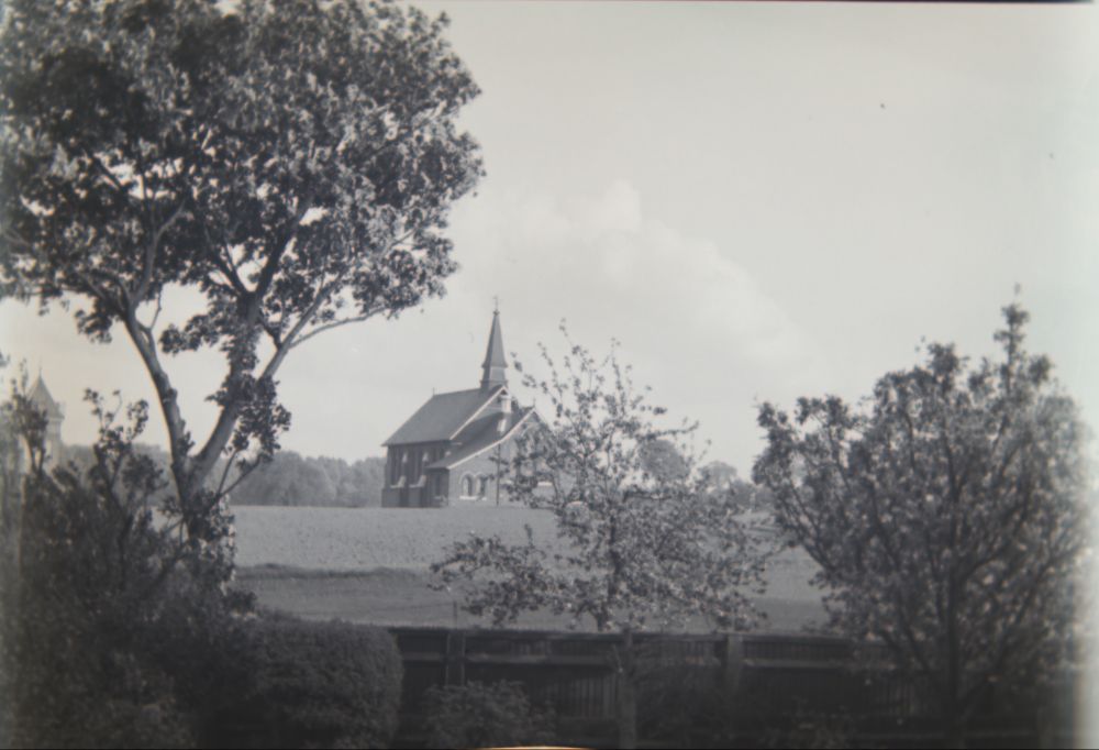 photo of a smallish chapel, simple gothic style, probably brick with small fleche, roughly three bay nave, with twin lancet windows separated by buttresses,  and broader chancel end with triple lancet window in centre.