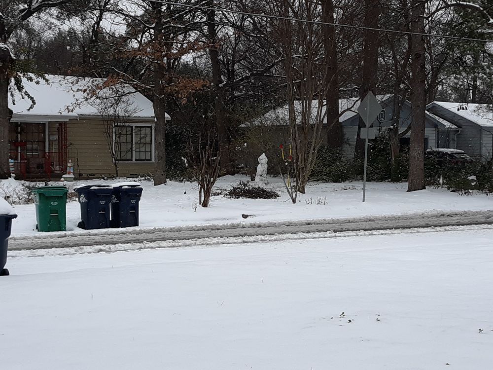 View of neighborhood covered in snow with a snowman built across the street.