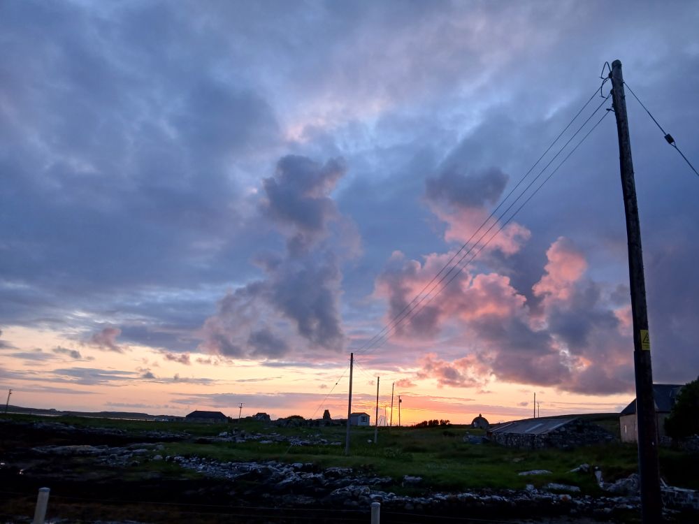 Black outline of buildings, orange stripes of firelit sky  blue and pink sunlit clouds above