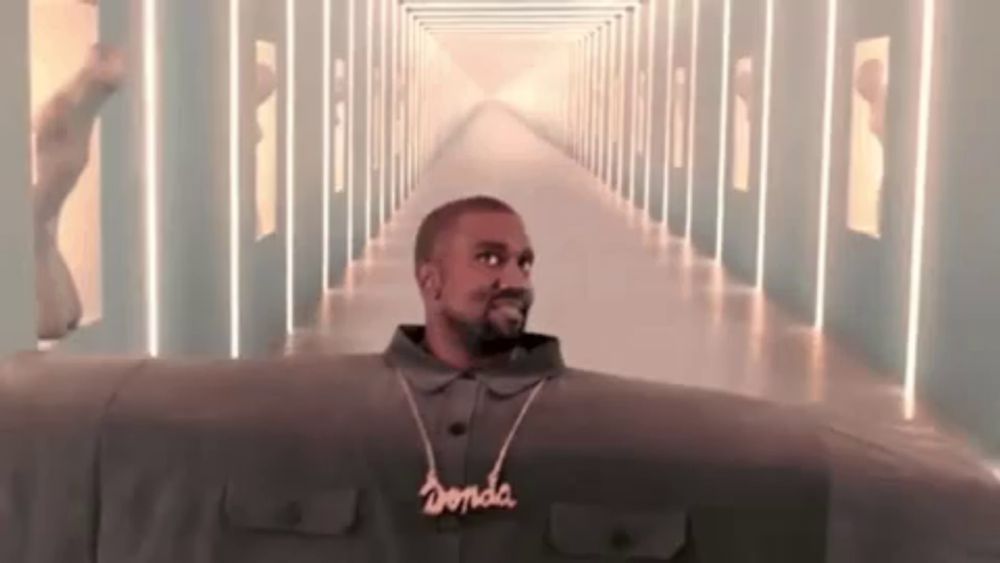 kanye west is standing in a hallway wearing a necklace and a jacket .