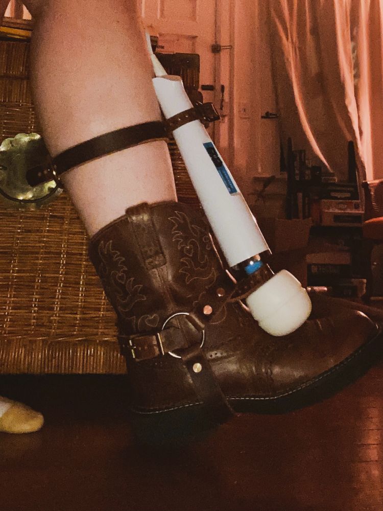 my right foot in a short brown cowboy boot with a brown leather boot harness holding a magic wand 