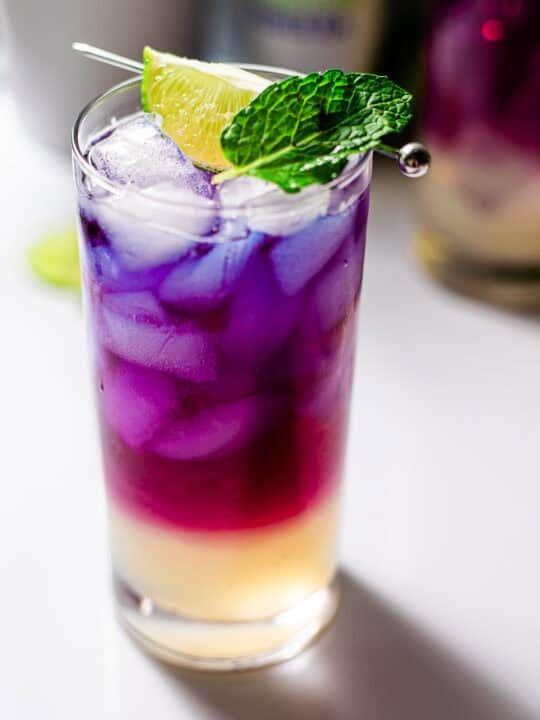 close shot of a butterfly pea flower lychee soda mocktail with mint and a lime