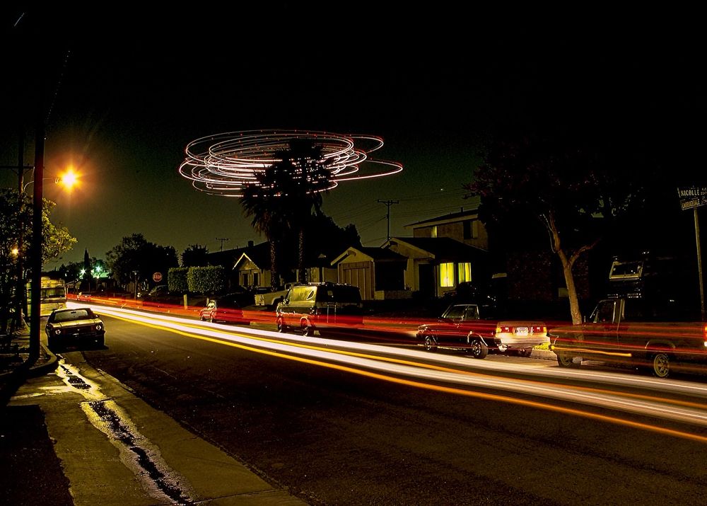 White swirls in a distant night sky over a residential street scene. Streaks from car lights in the foreground