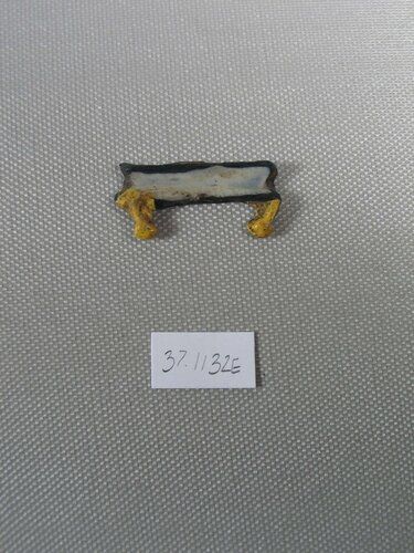 Glass inlay representing, in relief (rear surface flat), a high-prowed boat afloat on the water. The prows, which may be in the form of papyrus bundles, are opaque yellow. The remainder of the piece is opaque white with a border of translucent deep blue glass.  
 
Condition: Small scratches, some incrustation.